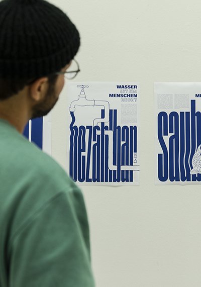 Mann mit grünem Pullover schaut sich typografische Arbeiten an der Wand an.