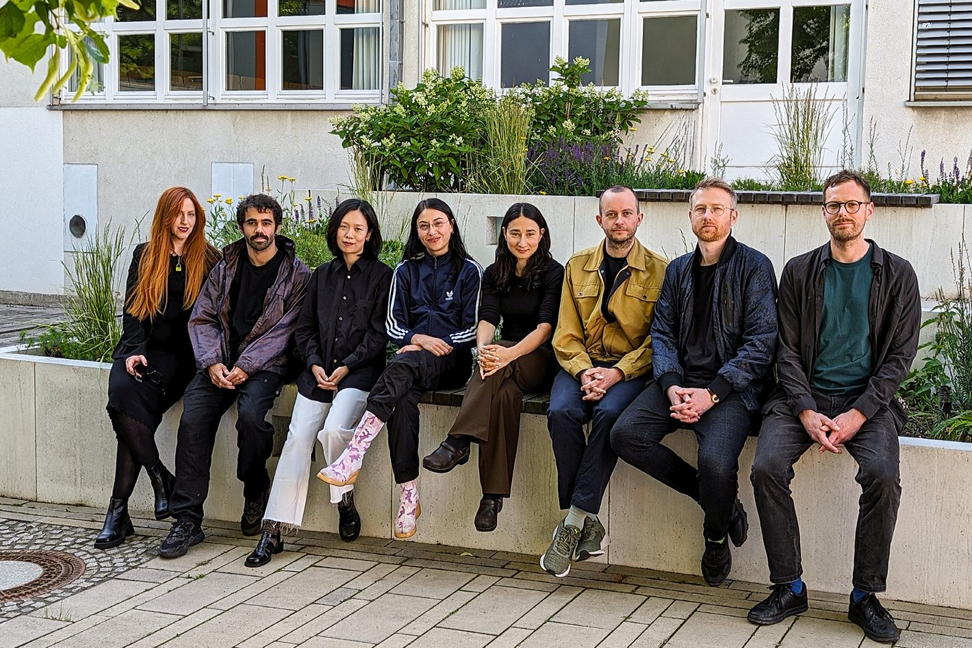 Acht Personen sitzen nebeneinander für ein Gruppenbild zusammen.