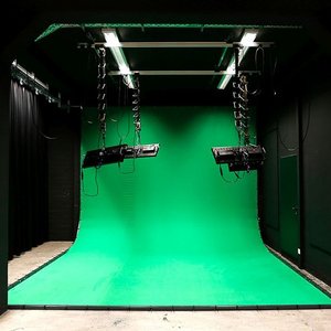 Ansicht auf ein Filmstudio. Ein Greenscreen wird von Deckenlampen ausgeleuchtet.