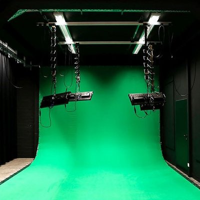 Ansicht auf ein Filmstudio. Ein Greenscreen wird von Deckenlampen ausgeleuchtet.