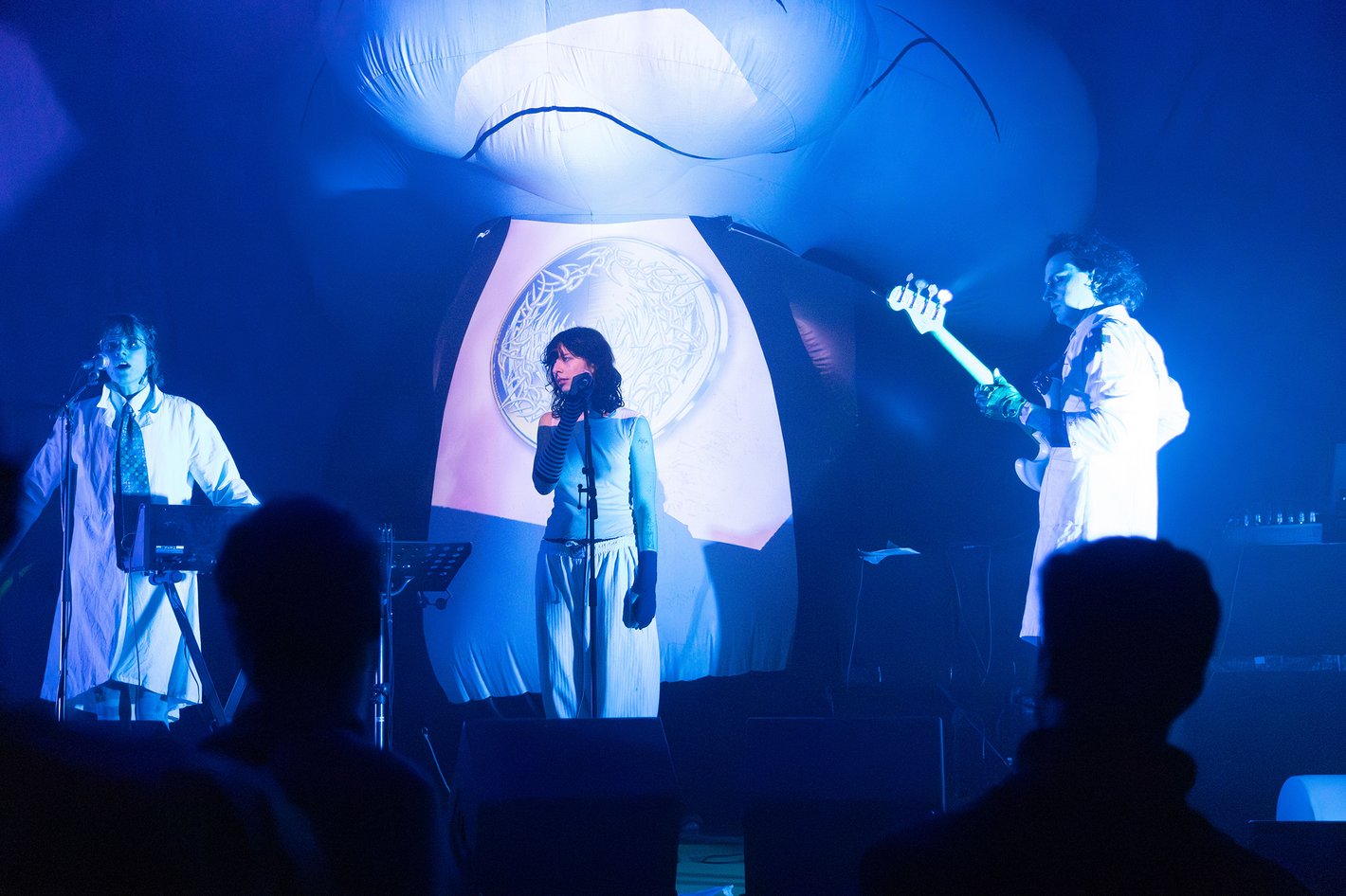 Drei Personen agieren auf der Bühne in blauem Licht.