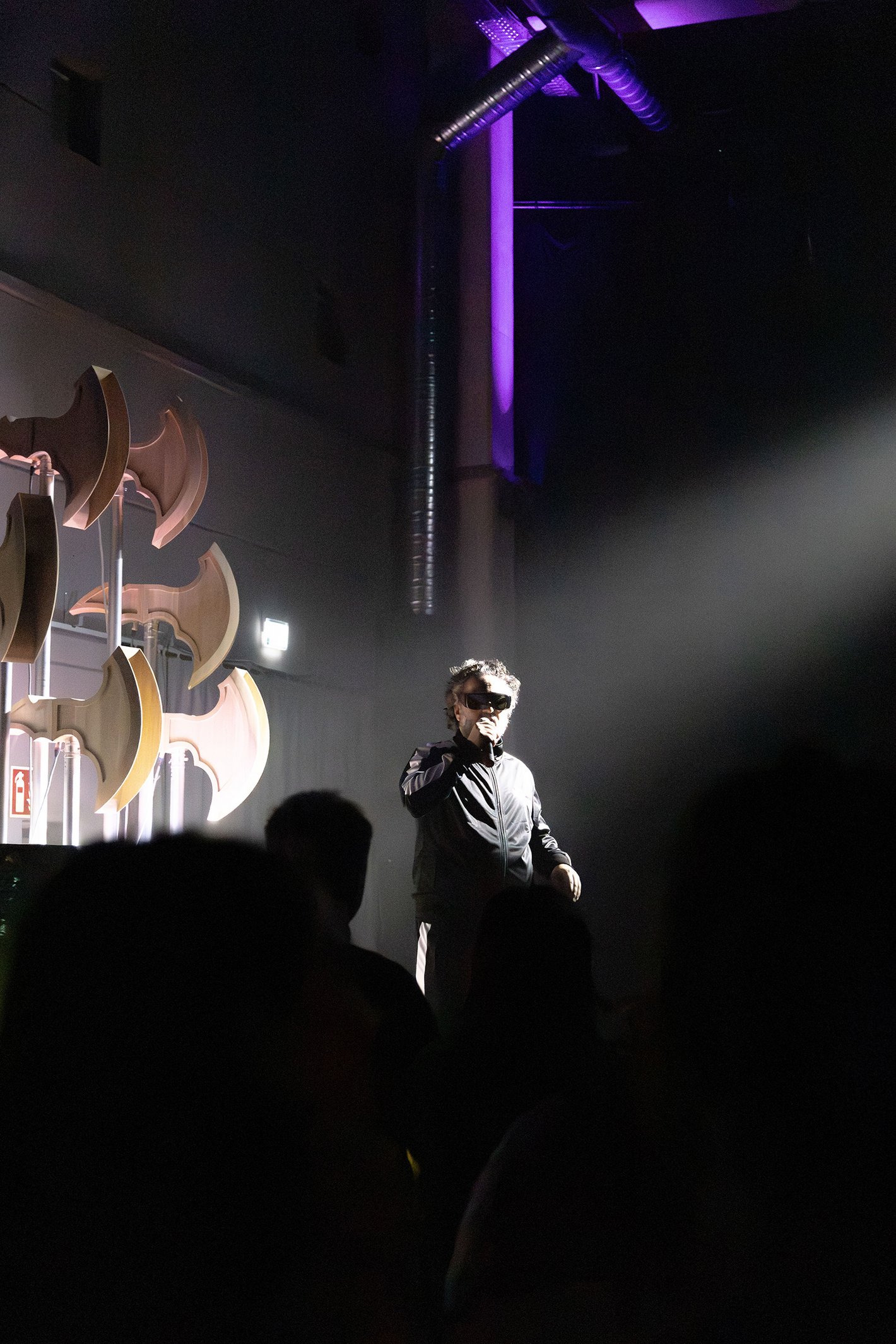 Ein Mann im schwarzen Trainingsanzug auf der Bühne spricht ins Mikrofon.