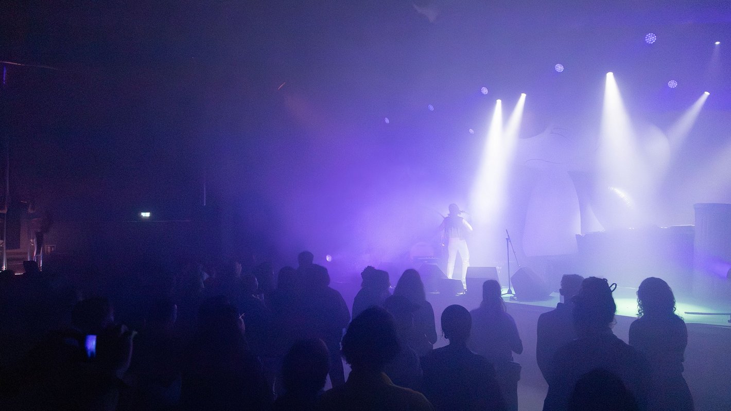 Publikum vor eine Bühne, in violettes Licht getaucht.